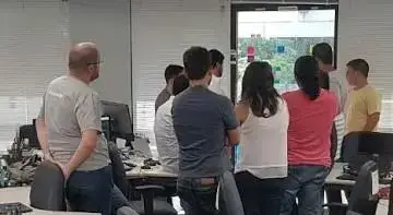 Pessoas em volta do Quadro de Tarefas realizando a reunião diária.