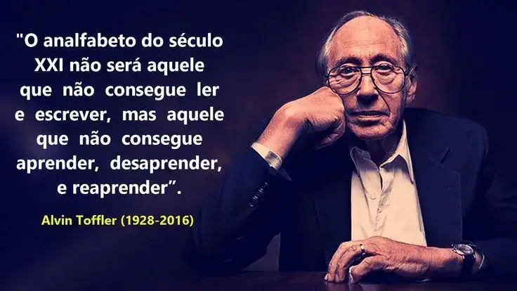 Alvin Toffler (1928-2016) um homem branco, cabelos grisalhos começando na metade da cabeça, vestindo uma camisa social branca e um paletó preto, ele está sentado com uma mão sobre a mesa, mostrando uma aliança no dedo e um relógio no pulso. A outra mão está apoiando seu queixo. Ao lado está sua frase: “O analfabeto do século XXI não será aquele que não consegue ler e escrever, mas aquele que não consegue aprender, desaprender, e reaprender”.